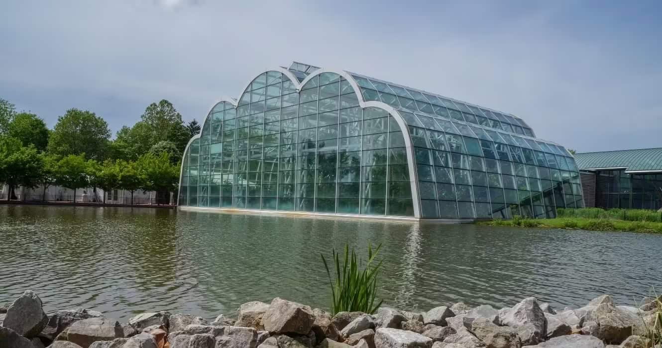 A lush, modern greenhouse with glass walls surrounded by water and greenery, showcasing innovative p.