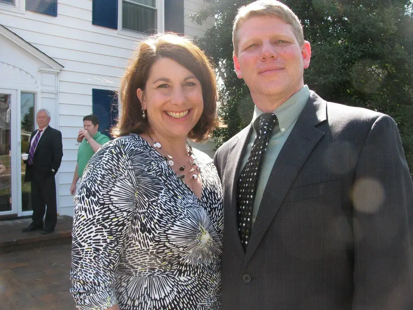 Two people smiling outdoors at a social event, dressed in business casual attire.