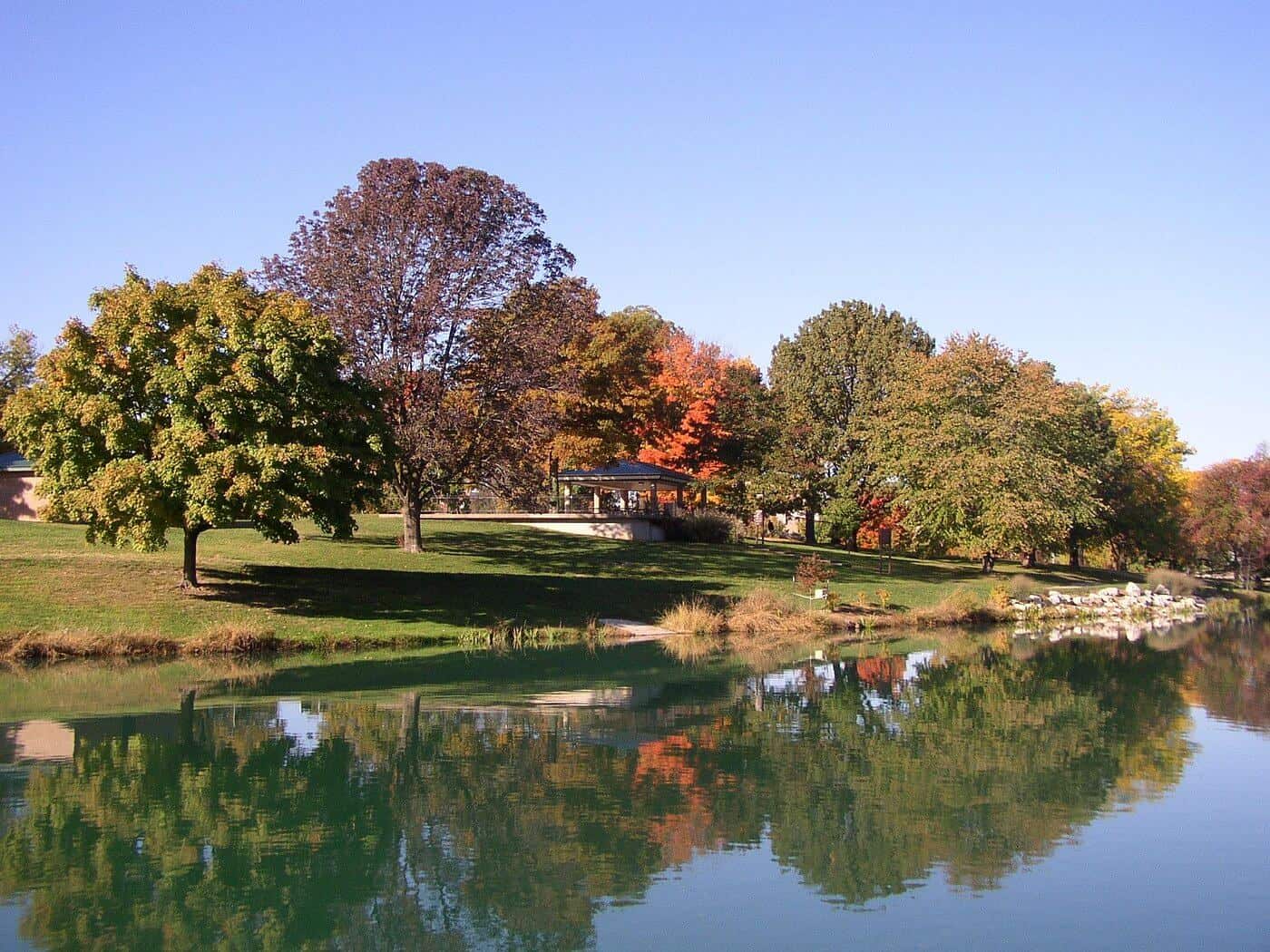 A lush park with colorful autumn trees reflected in a calm river.