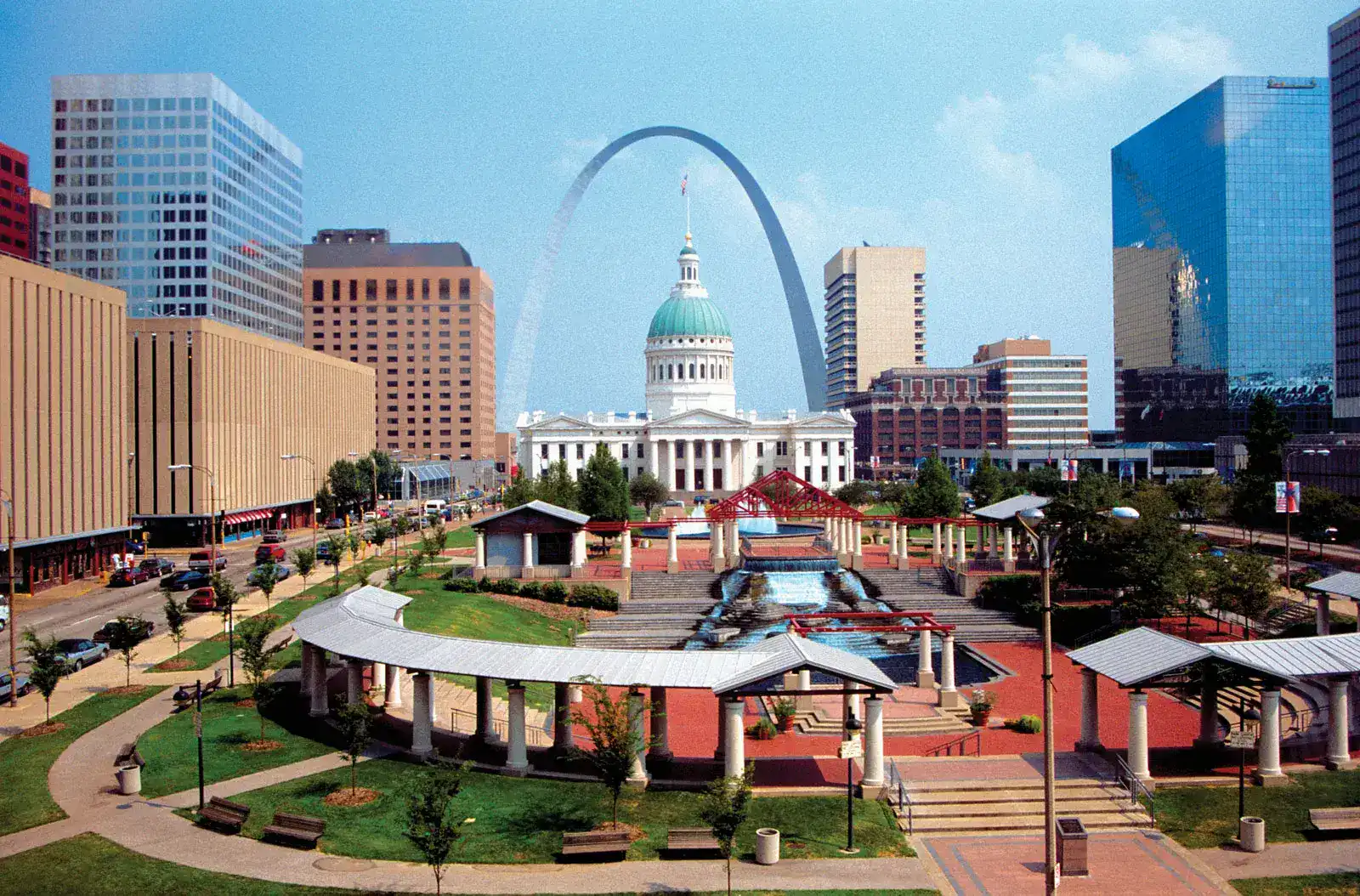 Bright cityscape featuring downtown St. Louis with Gateway Arch, historic buildings, and a park in t.