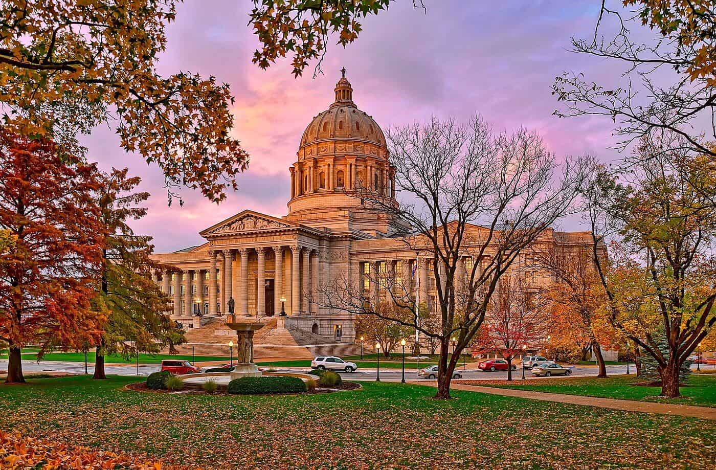 Historic capitol building with autumn trees and colorful sky in the background.
