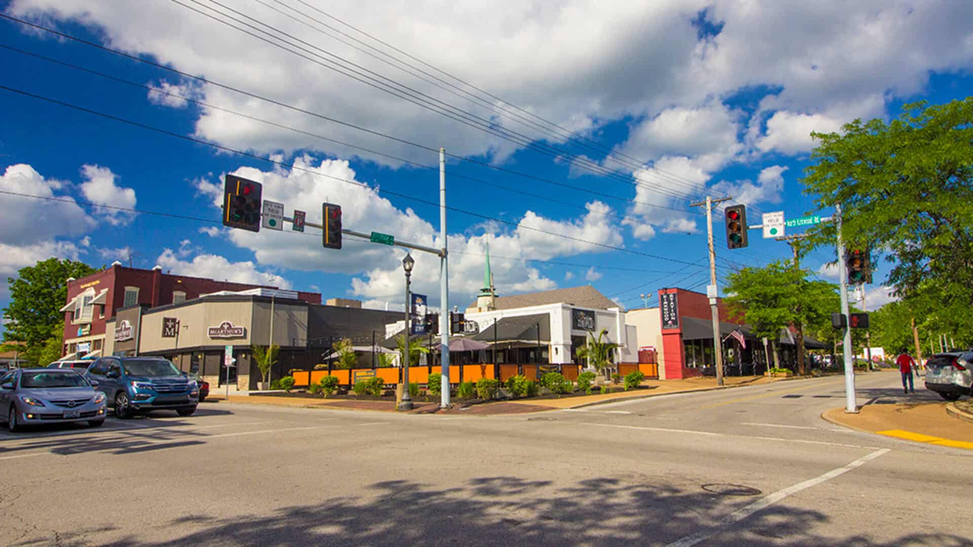 Bright city intersection with traffic lights, storefronts, and clear blue sky, showcasing urban envi.