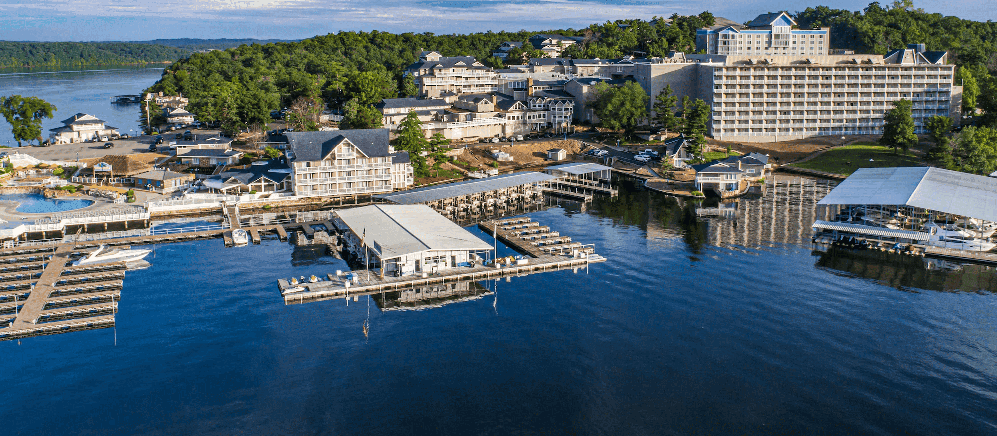 Aerial view of a luxury waterfront resort with multiple buildings, docks, and lush greenery surround.