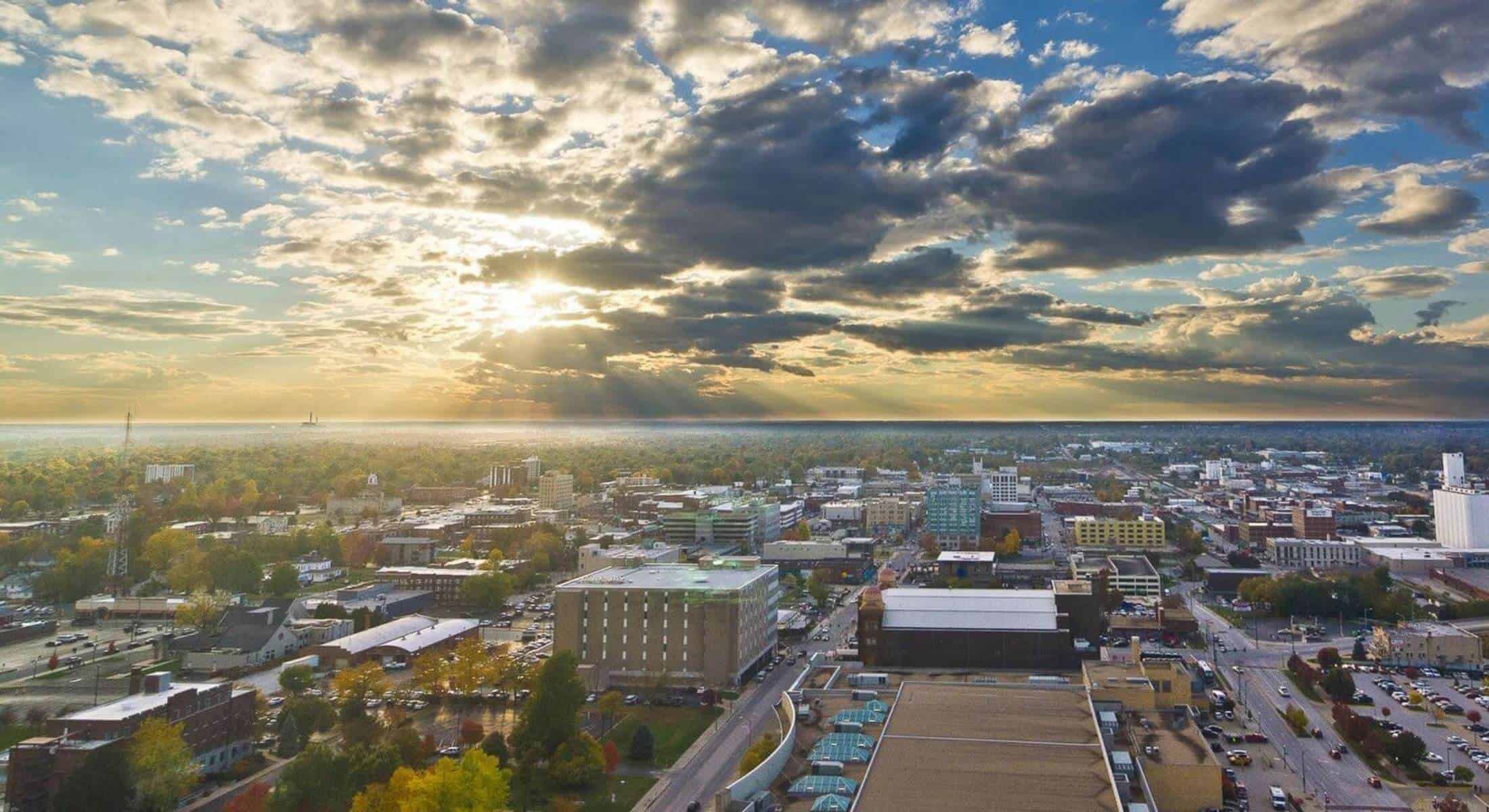 Aerial view of a cityscape during sunset with dramatic clouds and sunlight breaking through.