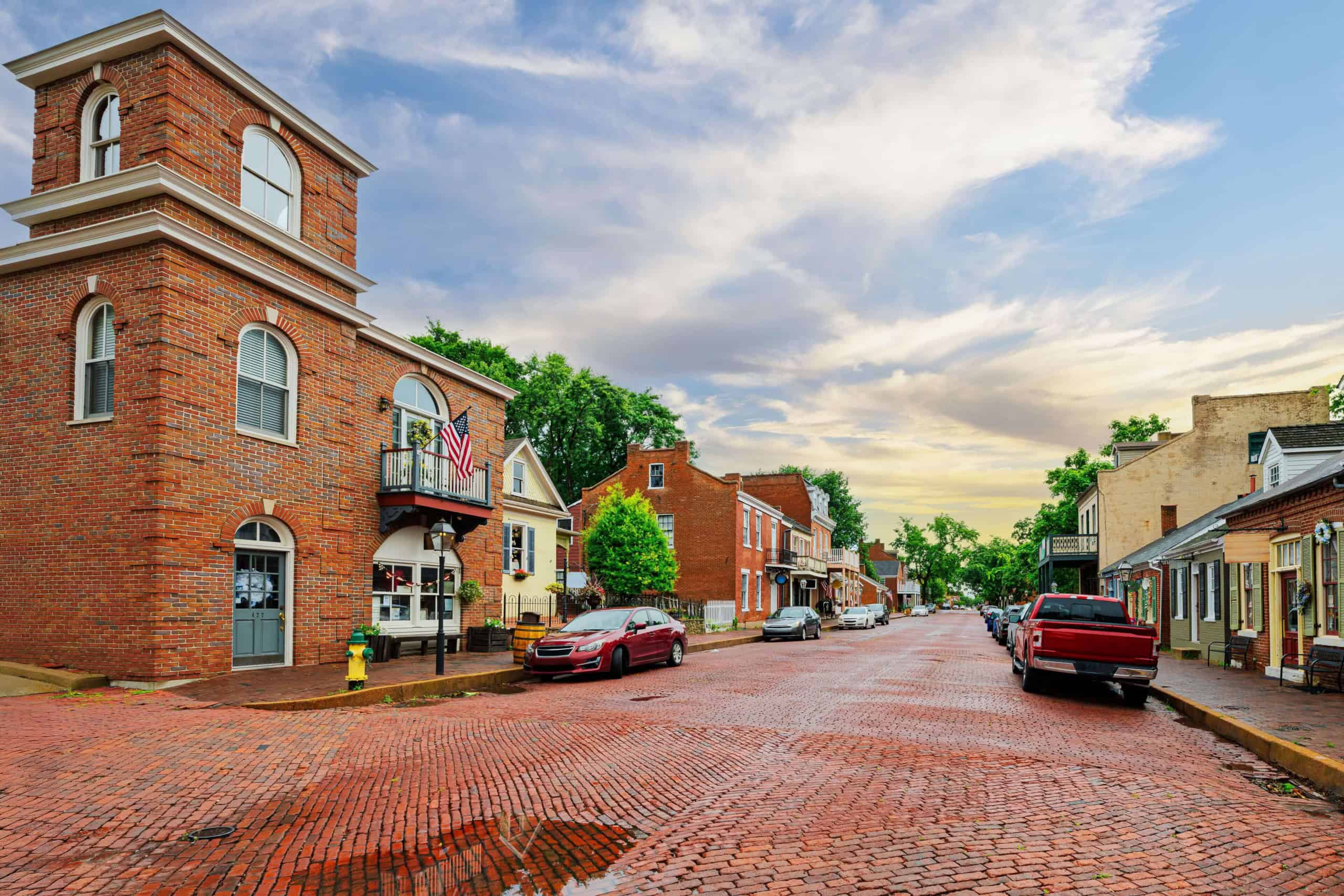Charming small-town street with brick buildings and parked cars under a partly cloudy sky.
