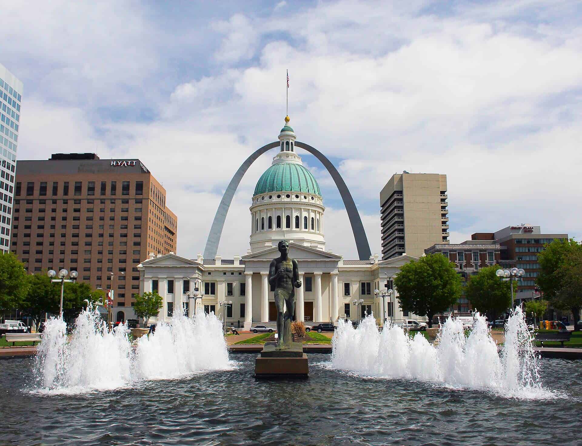 St. Louis City Hall with Gateway Arch in the background, fountain in foreground, sunny day.