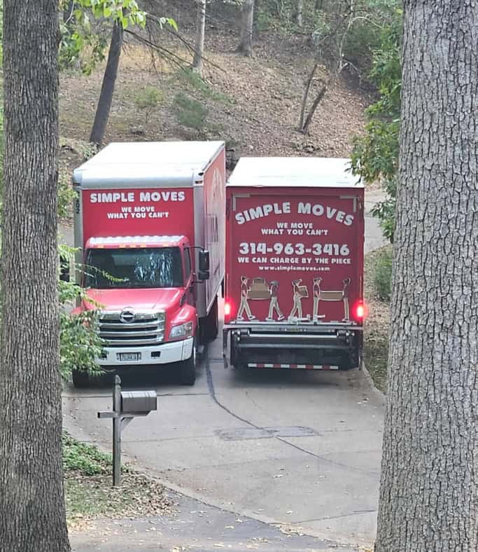 Moving truck and van from Simple Moves parked on a driveway in a wooded area.