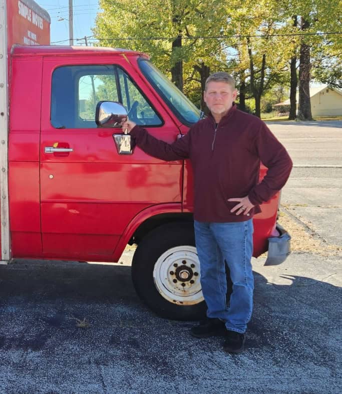 Man standing next to a red delivery truck holding a package.