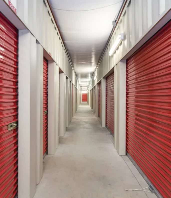 Storage unit hallway with red roll-up doors, clean and well-lit.